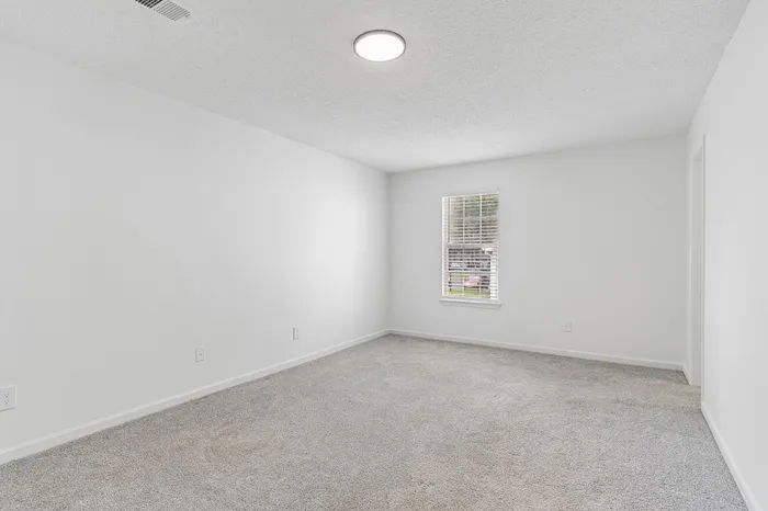 Bright, airy room with plush carpeting and large window, ideal for a cozy bedroom or office space.