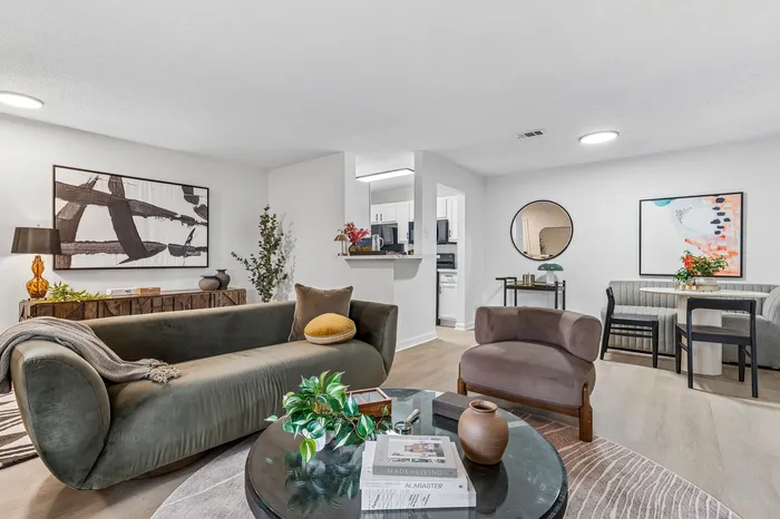 Elegant living space with modern furnishings, featuring a plush velvet sofa, stylish armchair, and chic dining area adjacent to an open kitchen.