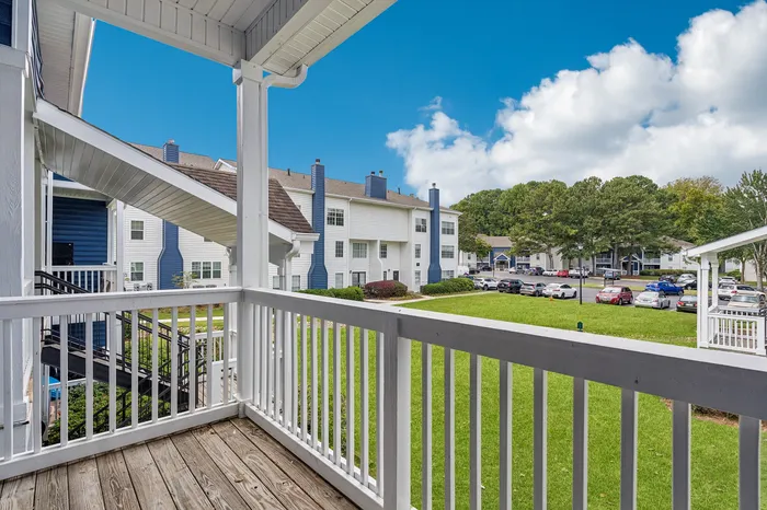 Charming balcony view overlooking a vibrant community with lush greenery and stylish apartment buildings under a bright blue sky.