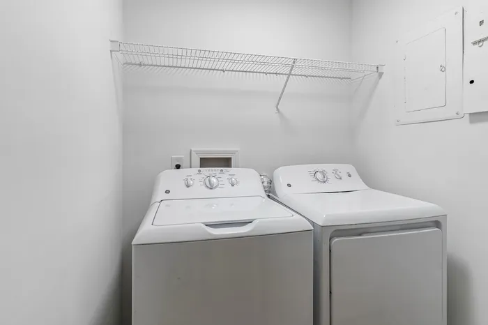 Modern laundry room with sleek white washer and dryer, complemented by a convenient overhead storage shelf.