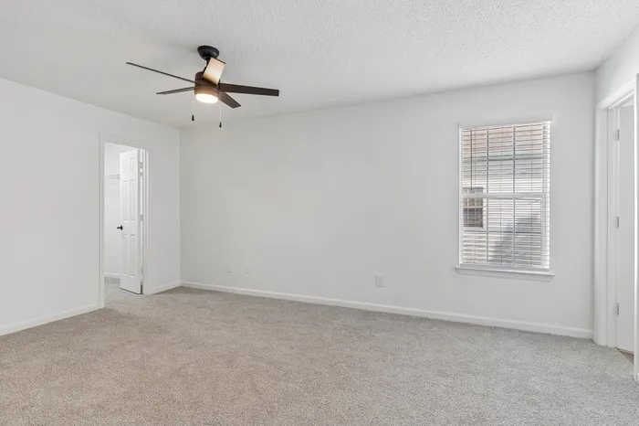 Bright and airy bedroom with plush carpeting, modern ceiling fan, and a window providing ample natural light.