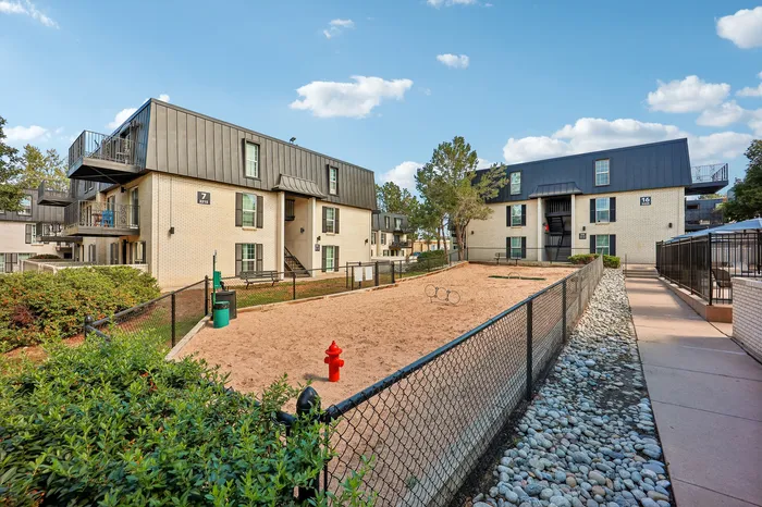 Charming apartment complex with modern architecture, featuring a spacious outdoor dog park surrounded by lush greenery and walkways.
