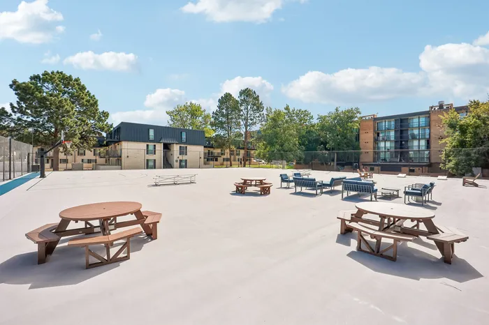 Spacious courtyard with picnic tables and lounge seating, surrounded by modern apartment buildings and lush greenery, perfect for outdoor relaxation.