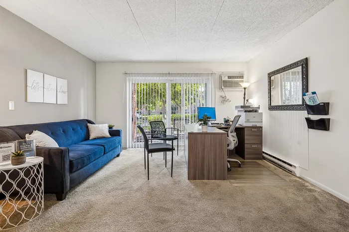 Modern living area featuring a plush blue sofa, sleek desk setup, and large windows with natural light in a stylish apartment.