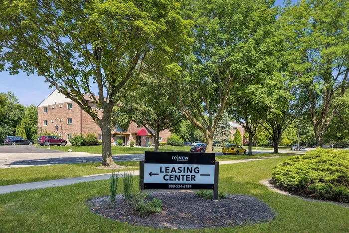 Inviting leasing center surrounded by lush greenery and charming brick apartments, offering a serene living environment.