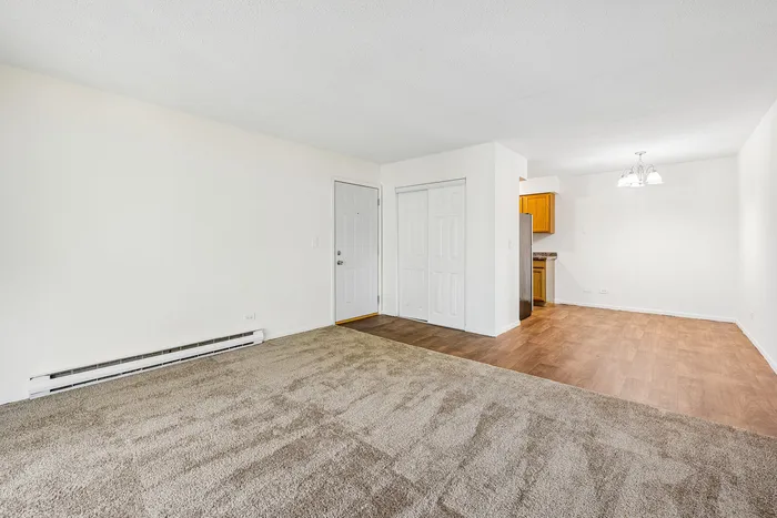 Spacious living area with plush carpet and laminate flooring, featuring a cozy dining nook and modern kitchen entrance.