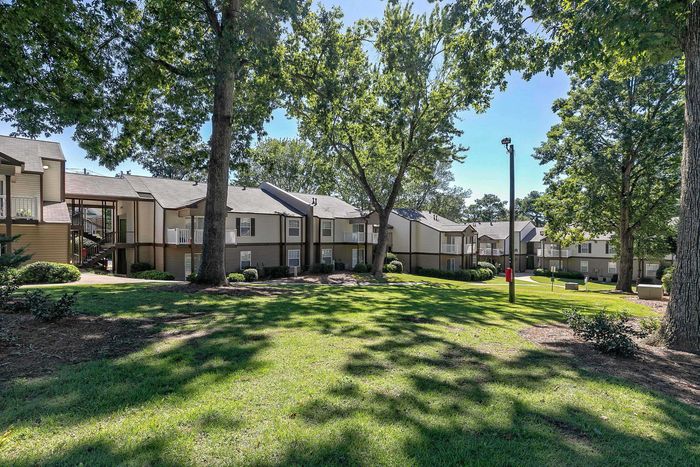 Charming apartment complex nestled among lush greenery with spacious lawns and inviting outdoor spaces.