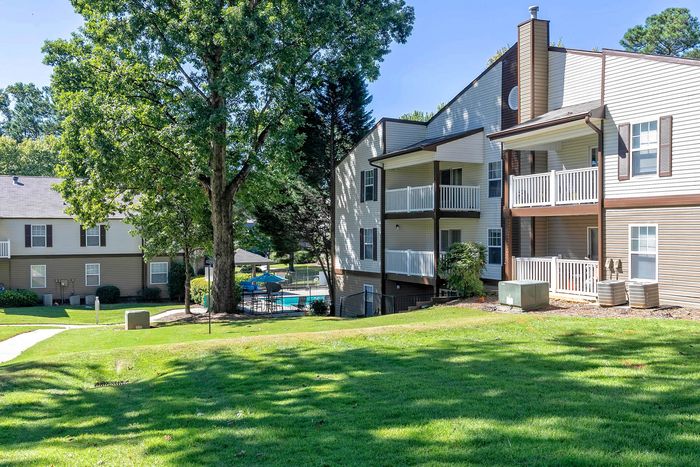 Charming apartment complex with private balconies, surrounded by lush greenery and a sparkling pool, inviting outdoor relaxation and modern living.