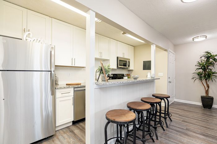 Modern kitchen with sleek stainless-steel appliances, elegant white cabinetry, and a stylish breakfast bar with wooden stools, perfect for entertaining.