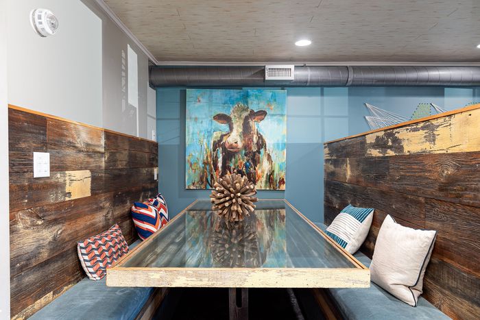 Charming dining nook with rustic wooden walls, stylish throw pillows, and a vibrant cow painting adding character to the space.