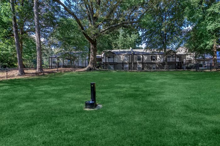 Inviting apartment complex nestled among lush trees, featuring a spacious green lawn and serene surroundings.