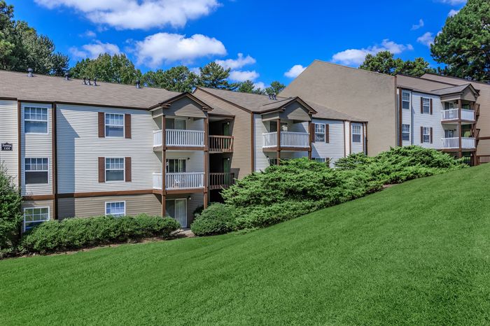 Charming apartment building with balconies and lush greenery, set against a bright blue sky, offering serene living in a vibrant neighborhood.