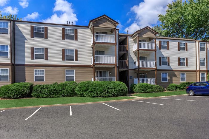 Charming three-story apartment building with private balconies and lush green landscaping under a clear blue sky.
