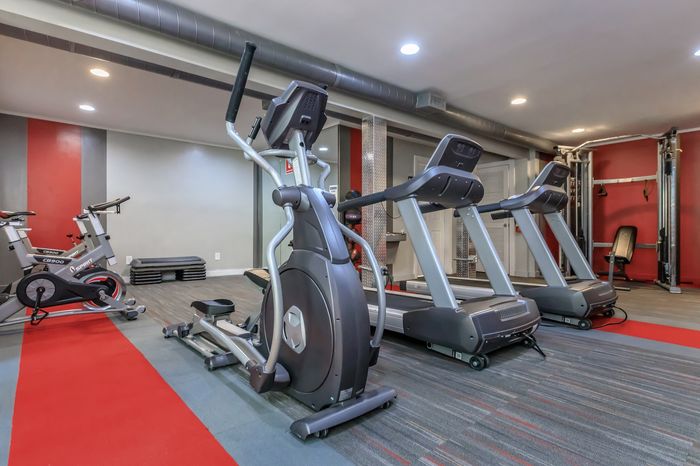 Modern gym featuring state-of-the-art ellipticals, treadmills, and exercise bikes on stylish flooring with vibrant red accents.