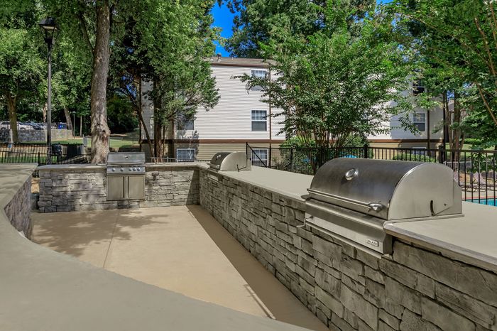 Charming outdoor barbecue area with modern grills, surrounded by lush greenery and stone accents, perfect for entertaining.
