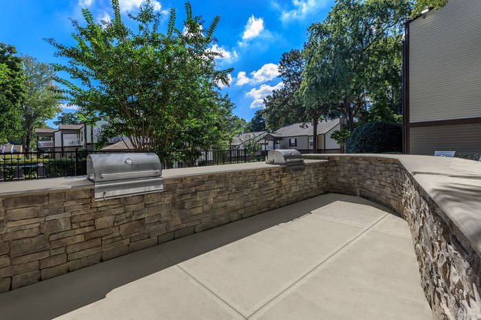 Inviting outdoor grilling area with modern stainless steel barbecue and stylish stone wall in a scenic residential setting.