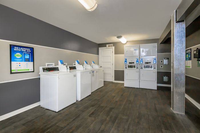 Modern laundry room with multiple white washing machines and dryers, featuring convenient app-controlled technology on a sleek wooden floor.