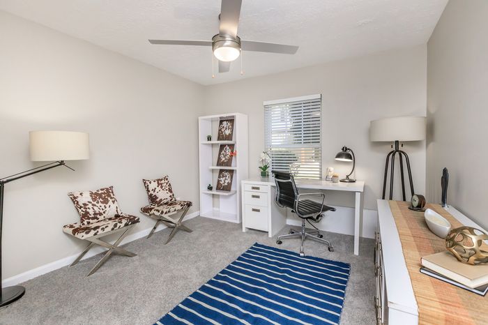 Modern home office with sleek design features, including a spacious white desk, elegant shelving, and chic cow-print chairs.