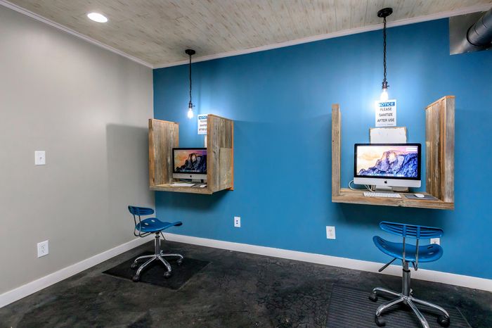 Modern workspace with two stylish wooden workstations, featuring iMac computers and vibrant blue chairs on a sleek concrete floor.