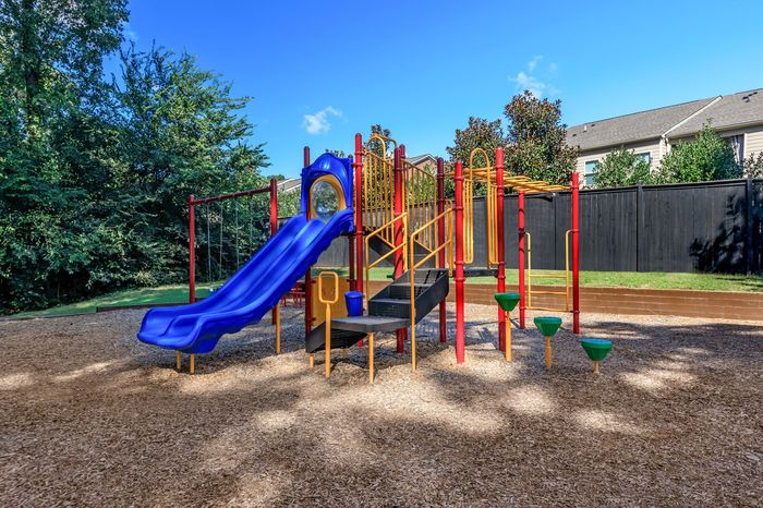 Lively playground featuring a vibrant blue slide, red climbing structures, and lush green surroundings.
