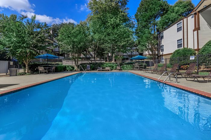 Inviting outdoor pool area surrounded by lush greenery and stylish apartment buildings, perfect for relaxation and leisure.
