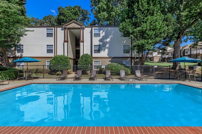 Charming apartment complex with a pristine outdoor swimming pool, surrounded by lush greenery and comfortable lounging chairs for relaxation.
