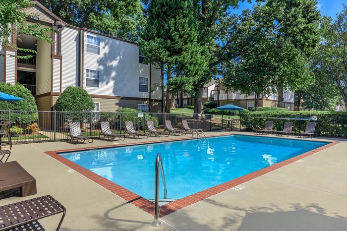 Inviting outdoor pool area with sun loungers surrounded by lush greenery and modern apartment buildings in the background.