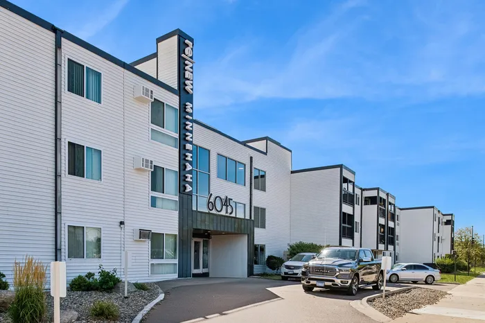 Modern apartment complex with sleek white facade and ample parking, showcasing urban living at its finest.
