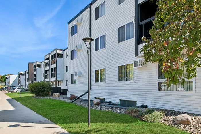 Charming modern apartment building with white siding, lush greenery, and ample parking in a serene neighborhood.