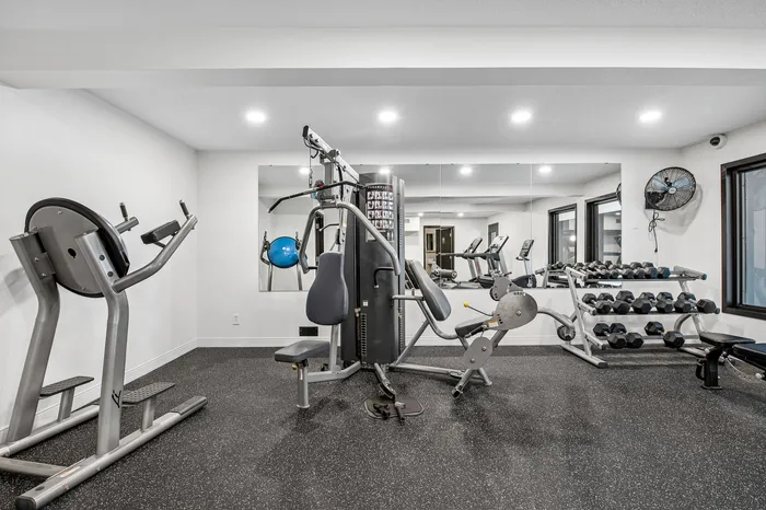 Modern apartment gym with state-of-the-art equipment, including weight racks and cardio machines, under bright lighting.