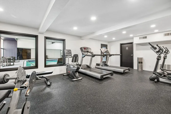 Modern and well-equipped gym overlooking an indoor pool with multiple cardio machines and ample space for workouts.
