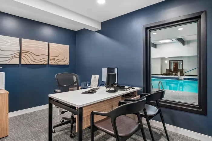 Modern office space with sleek decor, overlooking an inviting indoor pool area through a large window.