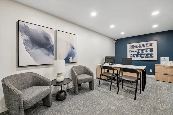 Modern office space with elegant gray chairs, abstract wall art, and a stylish desk area against a rich navy accent wall.