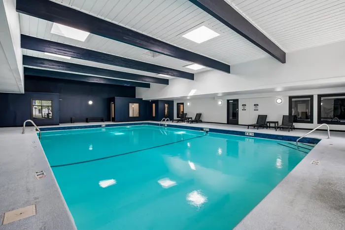 Spacious indoor swimming pool area with sleek modern design, featuring elegant lounging chairs and vibrant blue water, perfect for relaxation and fitness.