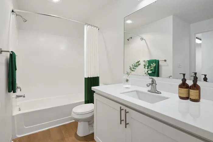 Modern bathroom with a sleek white vanity, large mirror, elegant glass vase, and stylish green accents.
