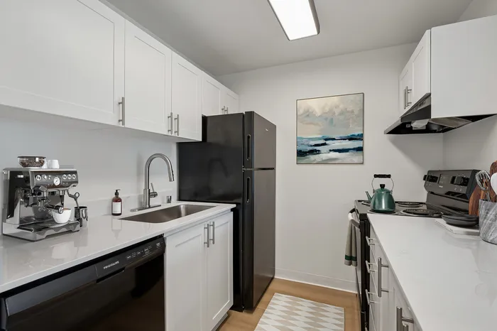 Modern kitchen with sleek white cabinets, stainless steel fixtures, and black appliances, featuring an espresso machine and artistic wall decor.