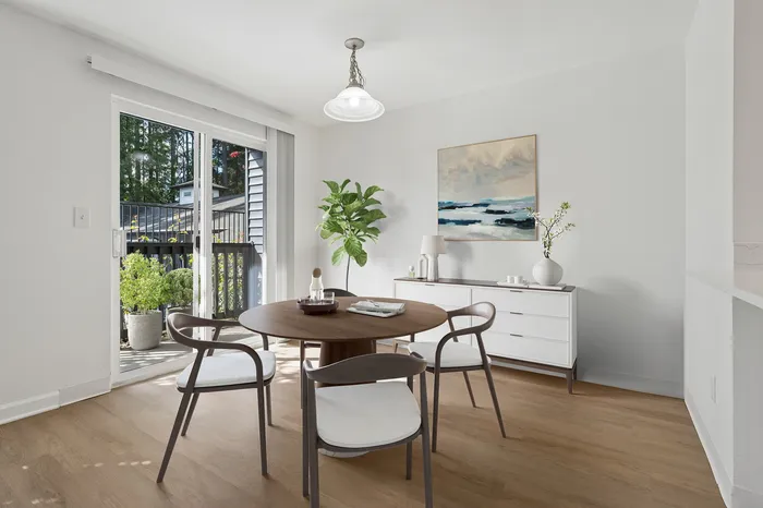 Bright dining area featuring a round wooden table with modern chairs, large sliding doors opening to a lush patio, and stylish decor enhancing a cozy, inviting atmosphere.