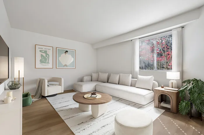 Elegant living room with modern decor, featuring a cozy white sectional sofa, stylish round coffee table, artwork, and a large window with natural light.