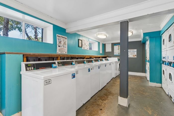 Bright and clean communal laundry room with multiple washers and dryers, enhanced by vibrant teal and white decor, offering a convenient and efficient laundry experience.