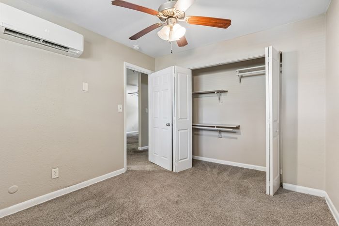 Cozy bedroom with soft carpet flooring, built-in closet shelves, and a modern ceiling fan.