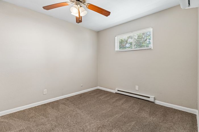 Bright, inviting bedroom with clean walls, cozy carpeting, and a ceiling fan; perfect for relaxation.