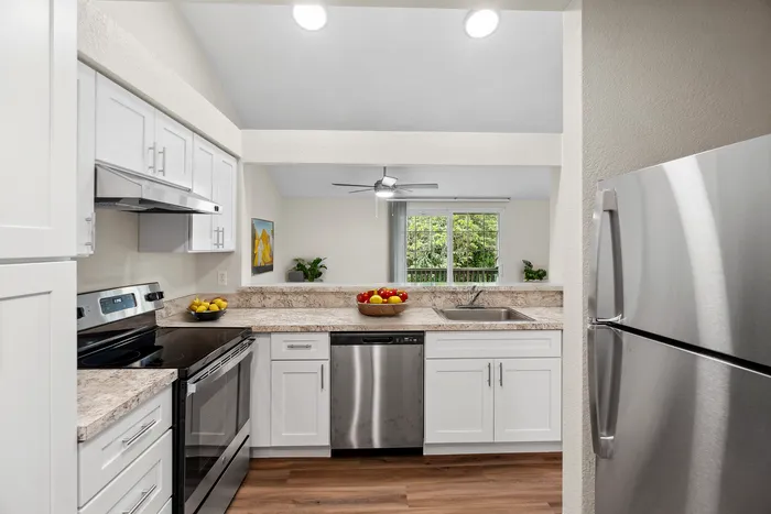 Contemporary kitchen with stainless steel appliances and white cabinetry, overlooking a lush view.