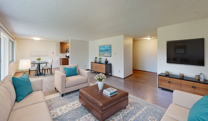 Bright open-plan living room with plush sofas, flat-screen TV, dining area, and modern kitchen.