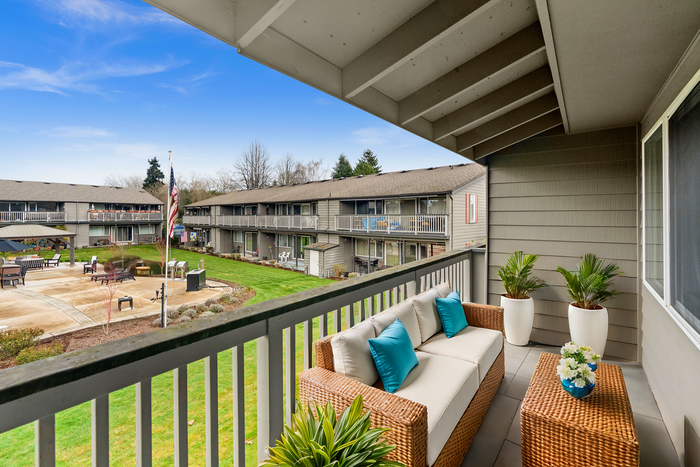 Cozy balcony with wicker furniture overlooks a vibrant courtyard surrounded by apartment buildings.