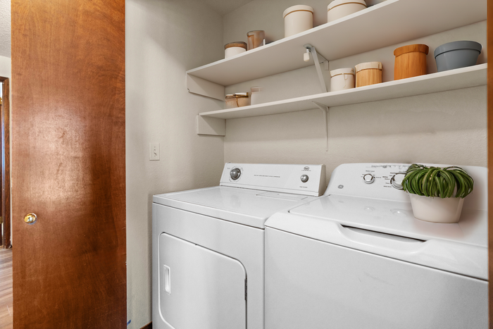 Modern laundry room with washer and dryer, shelving for storage, and decorative elements.