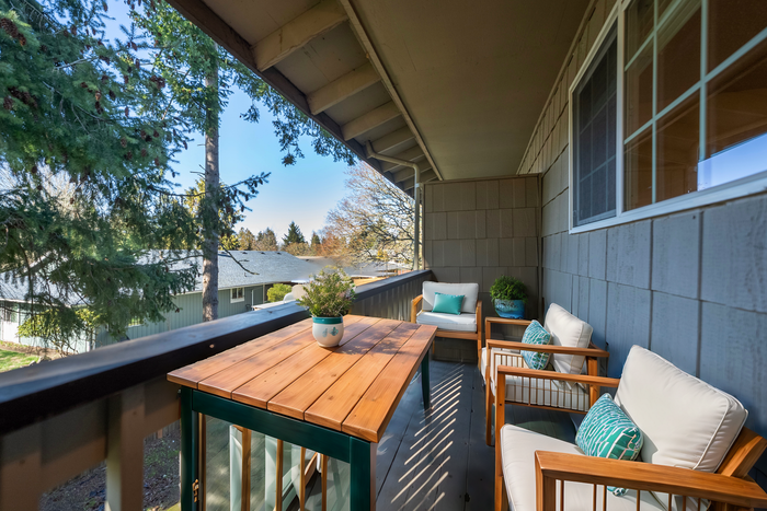 Inviting balcony with wooden furniture, cozy cushions, and lush greenery, overlooking a serene neighborhood view.