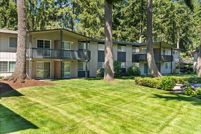 Charming two-story apartment building surrounded by lush greenery and tall trees.