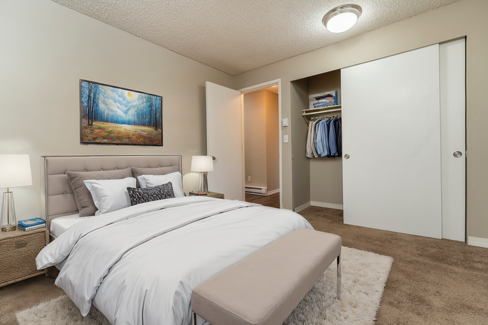 Inviting bedroom featuring a comfortable bed, elegant side tables with lamps, and an open closet with clothing neatly arranged.