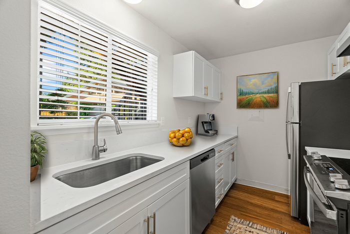 Contemporary kitchen with sleek white cabinets, stainless steel appliances, and a sunlit window.