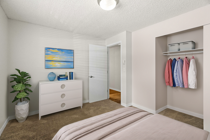 Inviting bedroom with modern decor, featuring a soft carpet, cozy bed, sleek dresser, and ample closet space with colorful jackets.